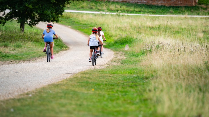 Three sisters ride bikes out into the sunny parkland at Ickworth Estate